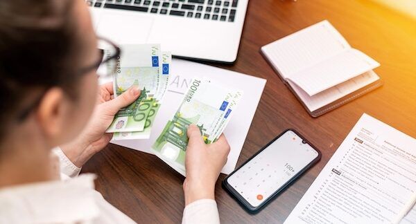 Donna che lavora nel settore finanziario contando denaro sul tavolo. Smartphone, blocco note.
