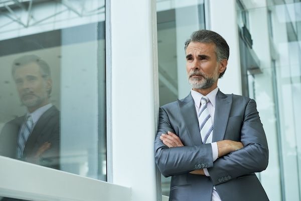 Piano medio dell'imprenditore in piedi con le braccia incrociate appoggiato al telaio della finestra.