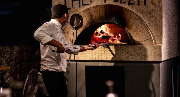 pizzaiolo nella parte posteriore sta preparando una pizza fatta in casa con un forno a legna.