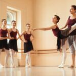 Ballerina di danza classica felice che balla con l'aiuto del suo istruttore mentre altre ballerine le osservano.
