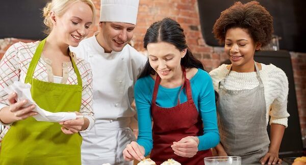 Concetto di scuole di cucina professionali, gastronomia, panificazione, cibo e persone - gruppo felice di donne e chef maschio che cucinano in cucina