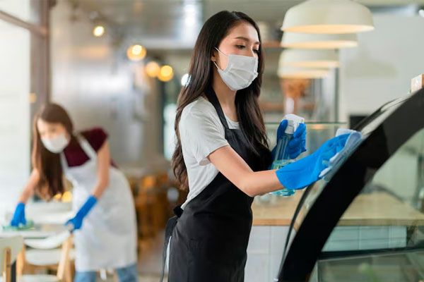 Personale giovane in grembiule e uniforme che spruzza detersivo o alcol sul bancone del prodotto